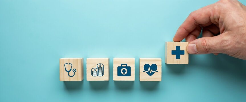 Hand placing a medical block on a row of health and finance wooden cubes on blue