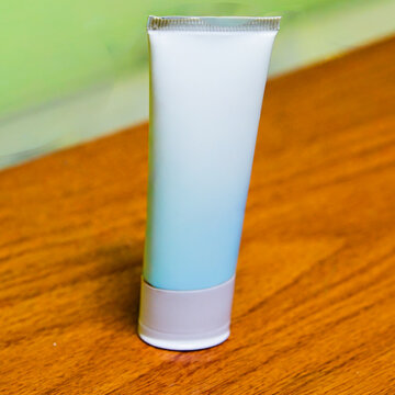 Unbranded plain white cosmetic tube packaging standing on a wooden table surface with a blurred green background, perfect for skincare product mockup.