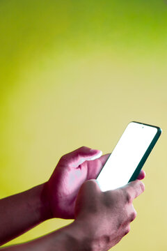 lose-up photo of a person's hand holding and using a smartphone with a glowing blank white screen for mobile application mockup on a green background.