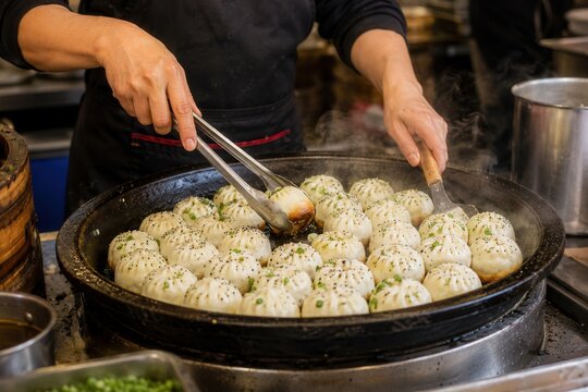 Goldbraun gebratene Sheng Jian Bao in der Pfanne, frisch gegart und dampfend serviert. Klassisches chinesisches Streetfood mit saftiger F&uuml;llung, handwerklich, herzhaft und beliebt.