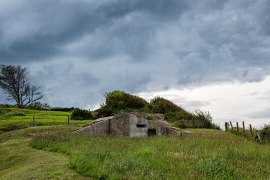 Historical WW2 German concrete bunker and MG nest at Wn 43 strongpoint on a green grassy hill in Arromanches, Normandy, under an overcast sky.