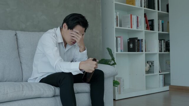 Depressed young Asian man addicted feeling bad drinking whiskey alone at home, stressed frustrated lonely drinking alcohol suffers from problematic liquor, alcoholism, life and family problems
