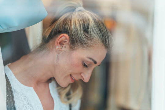Portrait of a blonde woman wearing a traditional Bavarian dirndl looking through the shop window of a Tracht store in Bavaria Germany.