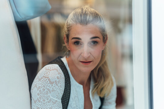 Blonde woman dressed in authentic Bavarian Tracht looking through the display window of a traditional clothing shop in southern Germany.