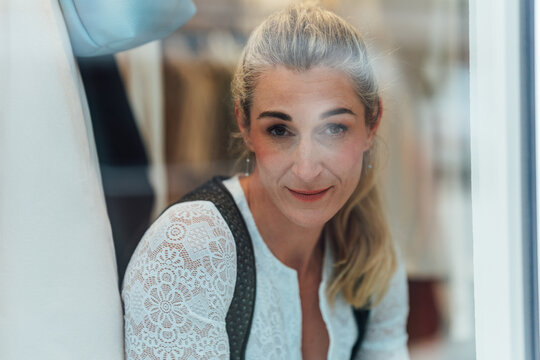 Portrait of a blonde woman in traditional Bavarian clothing looking through a Tracht shop window celebrating regional culture and fashion.