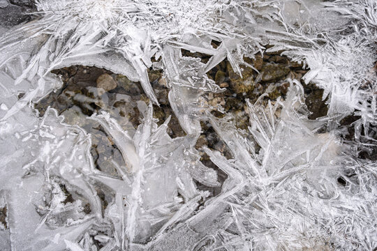 Close-up of intricate, sharp ice crystals frozen over a rocky riverbed in winter