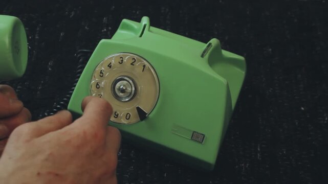 Anonymous caller dialing vintage green rotary phone on black surface