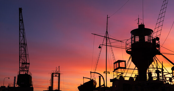 Ship deck and cranes in sunset silhouette view.