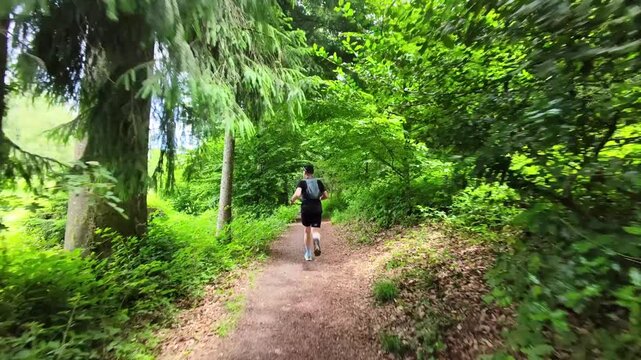 A solo trail runner follows a natural forest trail beneath a green canopy in Switzerland. Peaceful outdoor scenery highlighting fitness, adventure, and the enjoyment of nature.