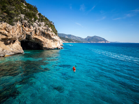 Aerial view of the limestone cliffs and sea caves of Cala Luna with a kayak paddling through the turquoise water in Baunei, Sardegna, Italy.