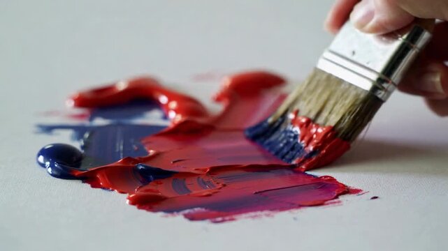Artist mixing red and blue paint on a white canvas. Close-up of paintbrush blending acrylic colors. Creative art process