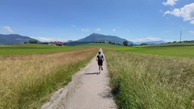 A trail runner follows natural paths through open meadows beneath a clear blue sky with views of Rigi and the Central Swiss mountains. Enjoying solitude, nature, and outdoor adventure in Switzerland.