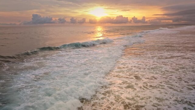 Green Bowl Beach in Bali, Indonesia, showcasing a calming sunset over the ocean with waves breaking on the shore, creating foam and reflections of golden sky. Nature background. Aerial drone flight