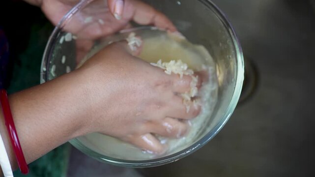 Hand washing white rice in a glass bowl over a kitchen sink. Woman hands preparing food for cooking. Healthy meal preparation process.
