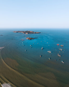 Aerial view of Sindhudurg Fort surrounded by the Arabian Sea with numerous fishing boats scattered across the water in Malvan, Maharashtra, India.