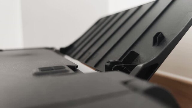 Close up of machine pulling paper from tray. Black corporate office printer performs automated task, pulling paper sheet into internal mechanism for fast document production. Concept office routine.
