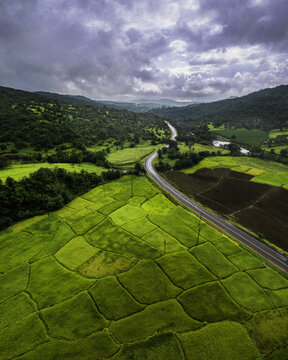 Aerial view of lush green rice paddies and agricultural fields bisected by a winding road through the hilly landscape of Karad, Maharashtra, India.