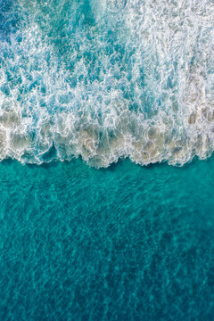 Aerial view of turquoise ocean waves crashing and creating white foam patterns in the clear water near the coastline of Torndirrup, Western Australia, Australia.