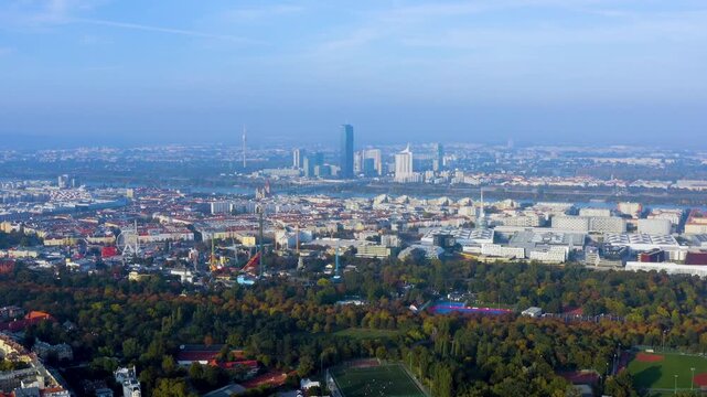 Aerial drone view of Vienna's Prater park and Wurstelprater amusement rides with the Donau City skyline, DC Tower, and Danube River behind in Vienna, Austria, autumn.