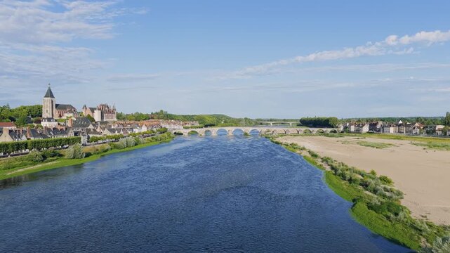 Aerial footage of the picturesque town of Gien in central France, showcasing the iconic stone arch bridge crossing the Loire River. The video captures the scenic riverside, traditional French