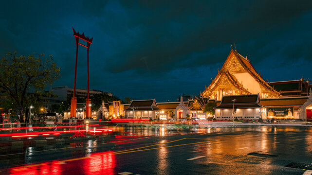Beautiful night view of the Giant Swing and Wat Suthat temple in Bangkok, Thailand with traffic light trails on a rainy night.