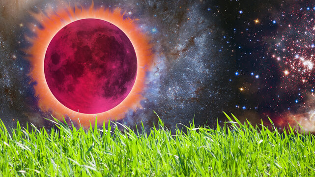 A bright pink moon is rising in the sky above a field of green grass. Many stars and galaxies are visible in the background. This moment captures a cosmic event.