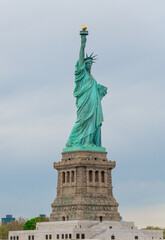 Fototapeta premium Statue of Liberty on Liberty Island, New York Harbor. Close frontal view of green copper statue holding torch aloft on stone pedestal, overcast gray sky, no base surroundings visible.