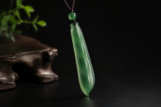 A slender green jade pendant shaped like a silique on a dark background.