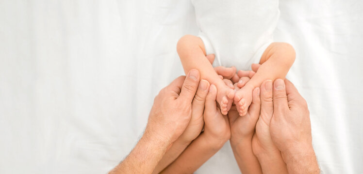 Close-up of a newborn baby's small legs in the arms of its parents and an older sister. Banner on the topic of care and parenting, and children's health