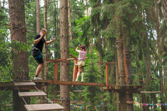 A girl and her father are walking on suspended bridges at high altitudes with obstacles. An amusement park and outdoor activities. Sports education for children
