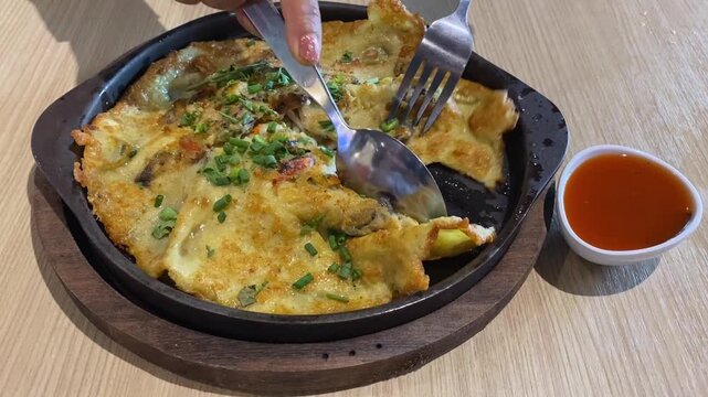 Mix & Stir Traditional Thai Crispy Fried Clam Mussel Seafood Omelette Pancake (Hoy Tod) Red Chili Dipping Sauce In Cast Iron Skillet with Fork & Spoon. Asian Food in Bangkok Street Food Restaurant