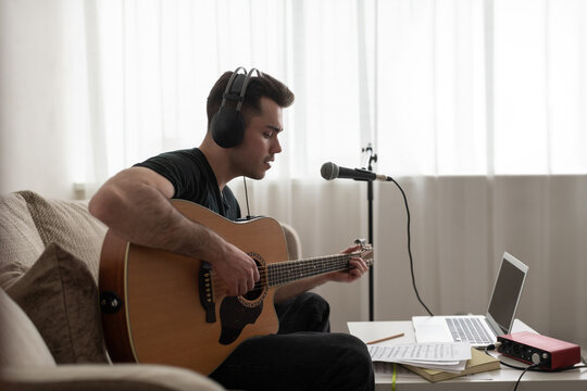 Male songwriter playing guitar on sofa.Man at home studio