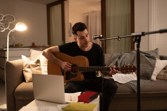 Male guitarist singing song on sofa. Man at home studio