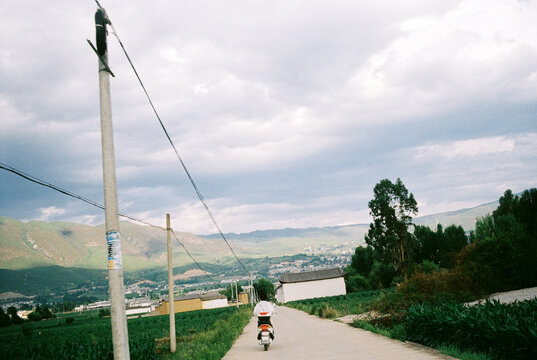 Person Riding a Scooter Down a Rural Road Toward Mountains