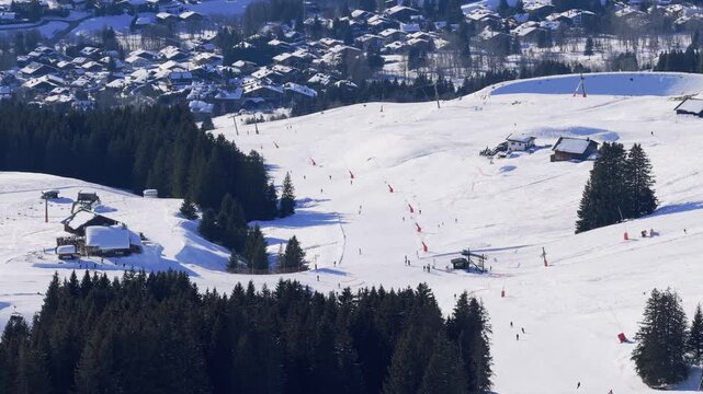 High-angle aerial footage of the Megeve ski resort in the French Alps, showing snow-covered ski slopes, ski lifts, chalets, and forested areas. The village of Megeve is visible in the background