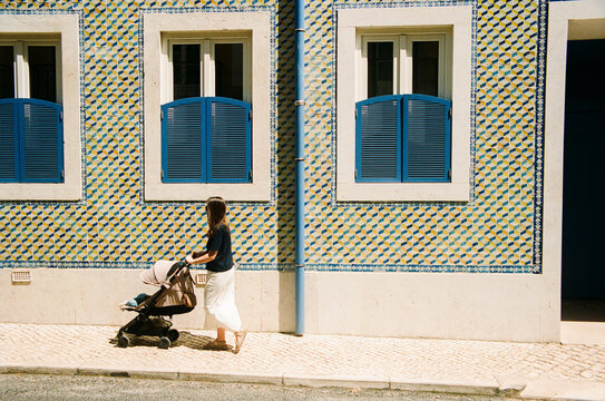 Person pushing stroller past tiled building film photo