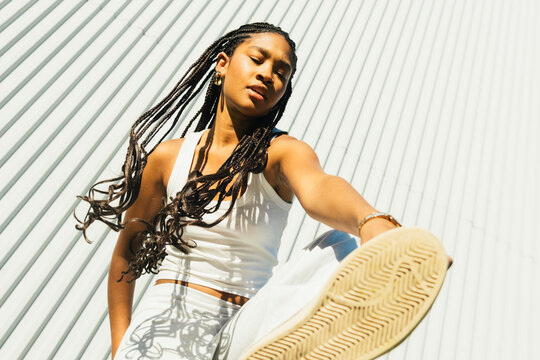 Young woman posing playfully with sneakers toward camera in urban sett