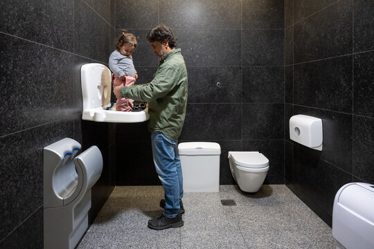 Father Helping Toddler On Public Baby Changing Table