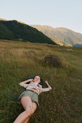 Obraz premium Relaxed woman lying in a grassy field with distant mountains, capturing a carefree outdoor lifestyle moment. Soft natural light creates a warm, tranquil mood and well being.
