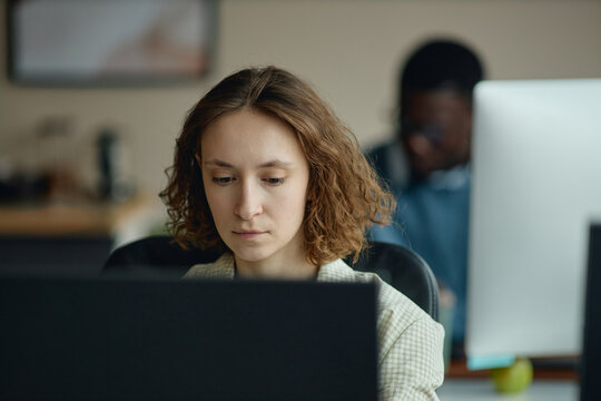 Young adult Caucasian woman working at desktop computer in office, focusing on screen during task management and productivity workflow. Ideal for business teamwork or workplace content