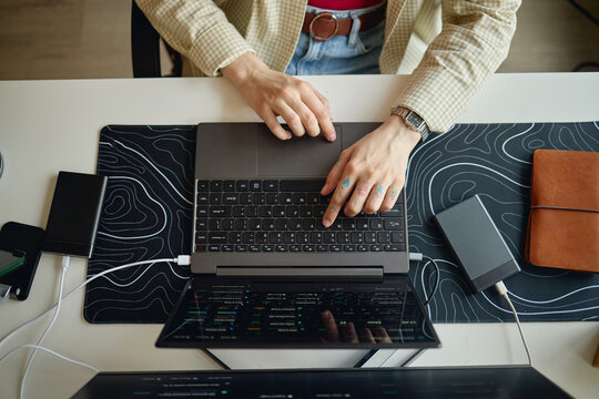 Overhead shot of young adult using laptop and external drive, typing code at desk. Technology workflow concept for software development, cybersecurity, remote work marketing