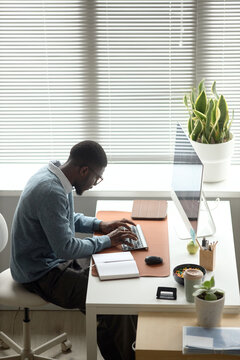 Young adult African American man typing at desktop computer in office, managing workflow and digital tasks. Ideal for business productivity, corporate communication, remote work