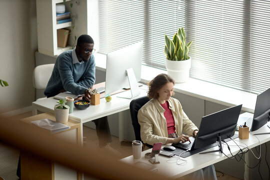 High angle view of African American man and Caucasian woman working at desktop computers in office, supporting teamwork, productivity, corporate communication use
