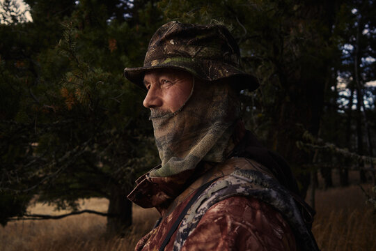 Hunter stands near trees with rifle at dusk in the forest