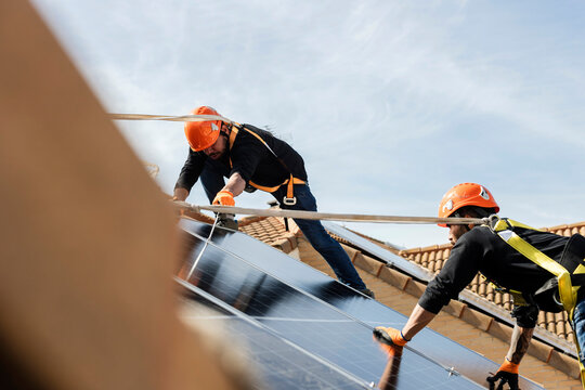 Workers installing solar panels on residential roof producing