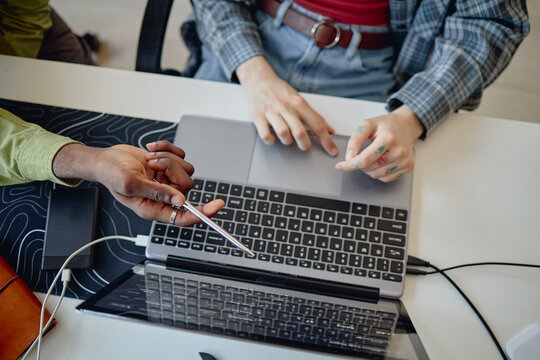 Overhead shot of coworkers collaborating on laptop, pointing at screen and reviewing digital workflow during meeting. Ideal for teamwork, project planning, tech support marketing