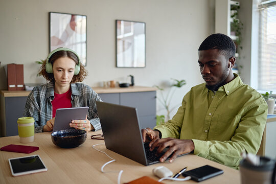 Young adult coworkers working on laptop and tablet at shared desk, supporting hybrid teamwork and digital productivity. Useful for remote work, startup, collaboration marketing