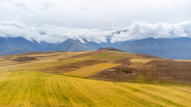 Aerial view of the agricultural landscapes of Cusco with patchwork fields and rolling hills under a cloudy sky in the Andes mountains, Cusco, Cusco, Peru.