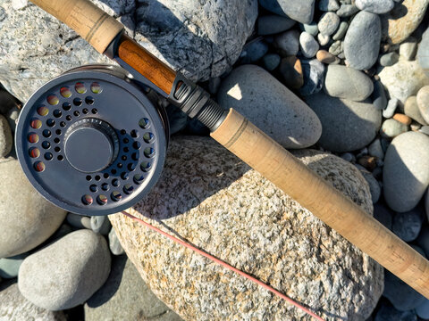Close up of fishing fly reel and rod on river stone rocks