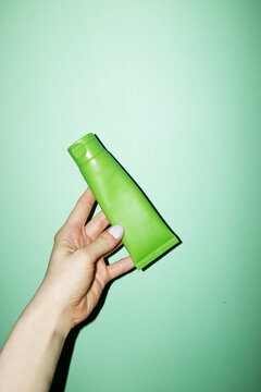 Hand holding a cosmetic beauty product green tube with lid with flash